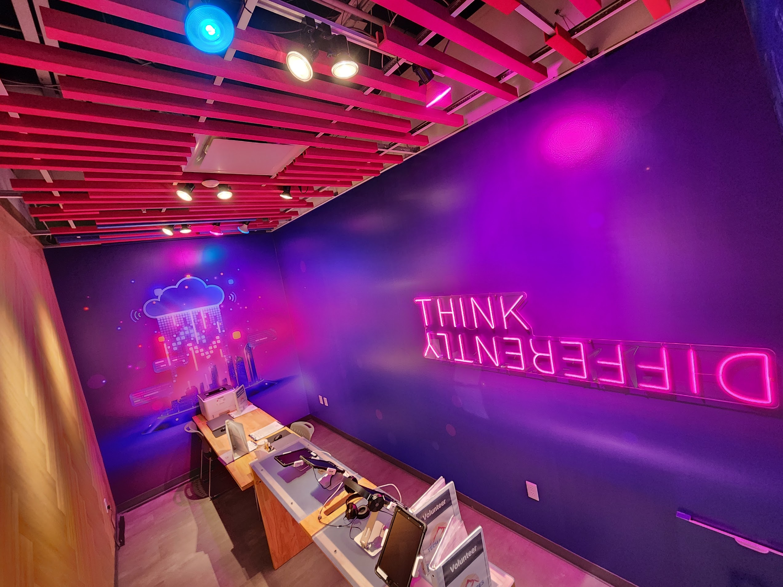Magenta slat ceiling, theatrical lighting, and the neon "Think Differently" wall